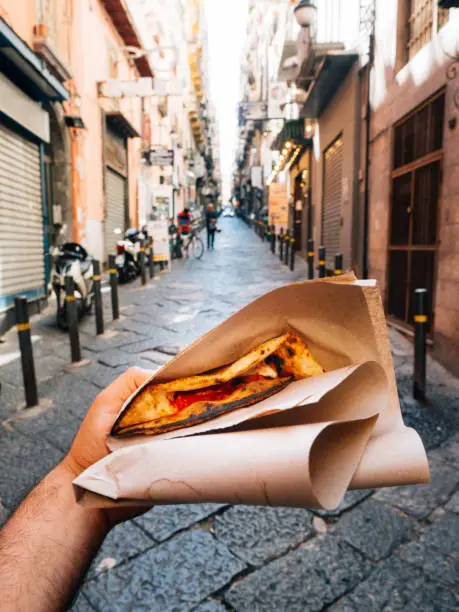 Pov view of a man eating a typical "Pizza a portafoglio" in Naples, Italy. The man is holding the wallet pizza.