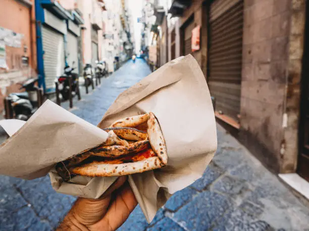 Pov view of a man eating a typical "Pizza a portafoglio" in Naples, Italy. The man is holding the wallet pizza.