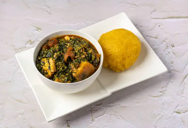 Popular okra soup served with garri on a white plate.