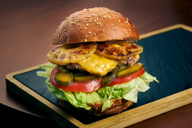 istock Beef burger with cheese, tomato, onion and pineapple on a black board. Fast food 1327486981