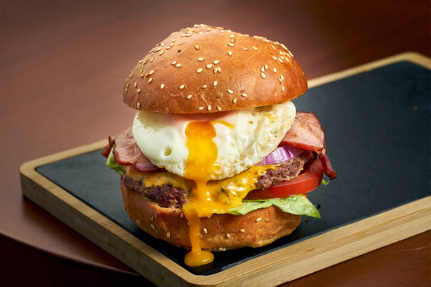 istock Beef burger with cheese, tomato, onion, bacon and egg on a black board. Fast food 1327486992