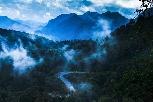 Scenery of mountain road in the morning mist. Stunning view of curves mountain road in foggy, rain clouds covers mountains range in the backgrounds. Tourism, road trip, holiday concepts. Soft focus.