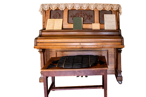 Vintage upright piano over a hundred years old with ornate panels and a lace doily on top and hymnals sitting on it isolated on white