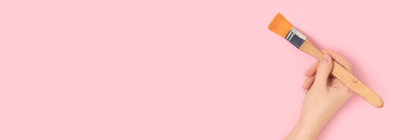 istock Female hand hold paintbrush on a pink pastel background. 1327492934