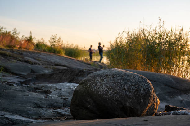 A closeup of a rock standing on the shore. Two out of focus fisherman in the background. stock photo
