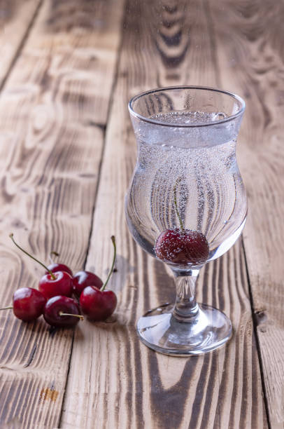 un vaso de agua fresca con gas con una cereza sobre un fondo de madera. bebidas refrescantes en climas calurosos - soft cider fotografías e imágenes de stock