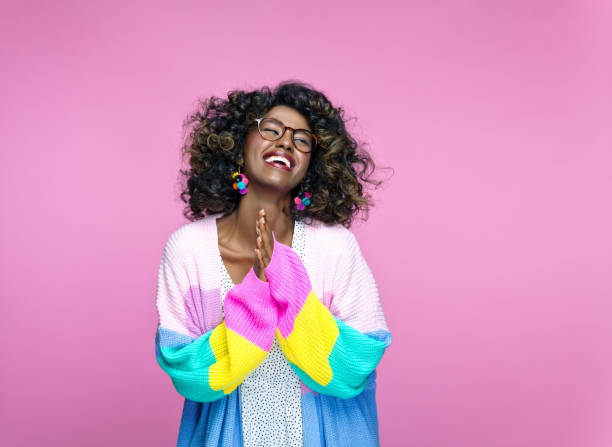 Excited woman wearing rainbow cardigan Cheerful african young woman wearing rainbow cardigan looking up and laughing. Studio portrait on pink background. girl power photos stock pictures, royalty-free photos & images