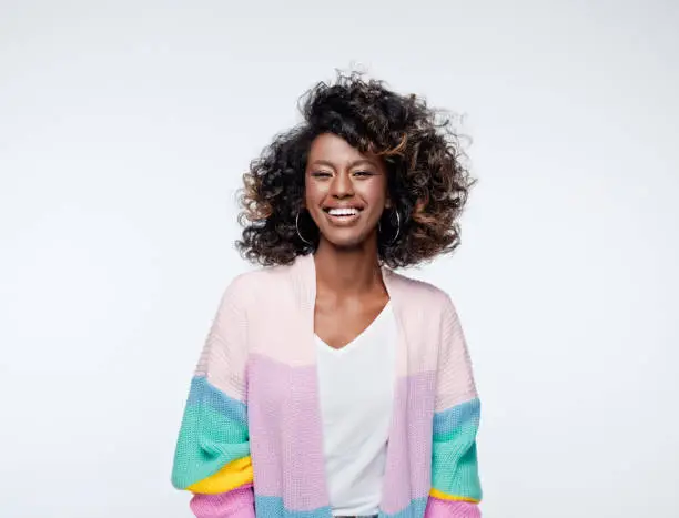 Cheerful african young woman wearing rainbow cardigan laughing at camera. Studio portrait on white background.