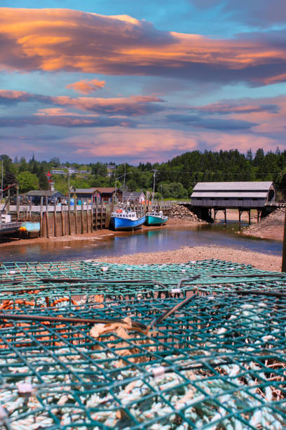 Fishing wharf in St. Martins, New Brunswick, Canada on low tide with  boats in mud, a covered bridge in the background and lobster traps in front and beautiful sunset and clouds Fishing wharf in St. Martins, New Brunswick, Canada on low tide with  boats in mud, a covered bridge in the background and lobster traps in front and beautiful sunset and clouds st. martins stock pictures, royalty-free photos & images
