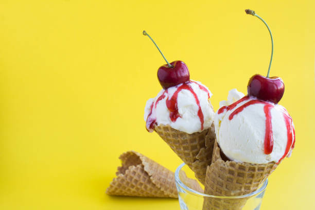 Close-up on vanilla ice cream in a waffle cone with cherry on the yellow  background. Copy space.