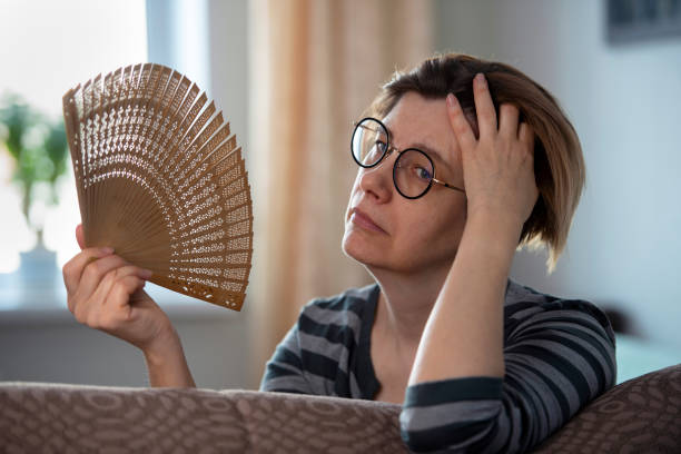 Exhausted middle aged woman waving her fan, suffering from menopausal symptoms, experiencing hot flush. Close-up portrait of pretty mature woman. inside of flash stock pictures, royalty-free photos & images