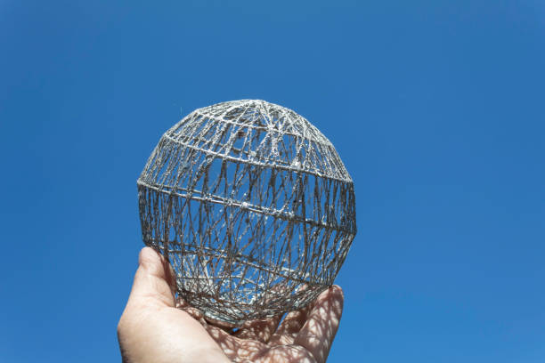 Against the blue sky, the hand holds a ball similar to a model of the Earth.