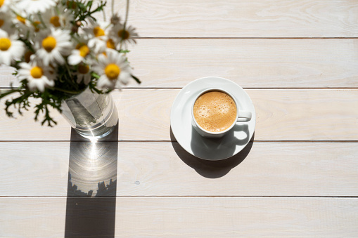 cup of coffee with daisy on white wooden. Close-up.