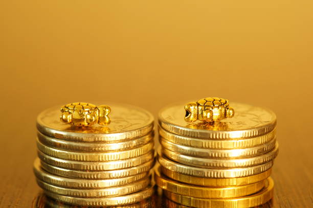 istock Two metal turtles with coins on a gold background. 1327517431