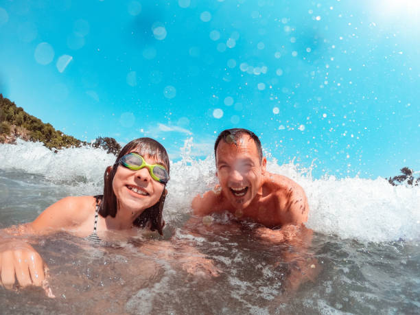 istock Father and daughter getting splashed by the sea wave 1327522602