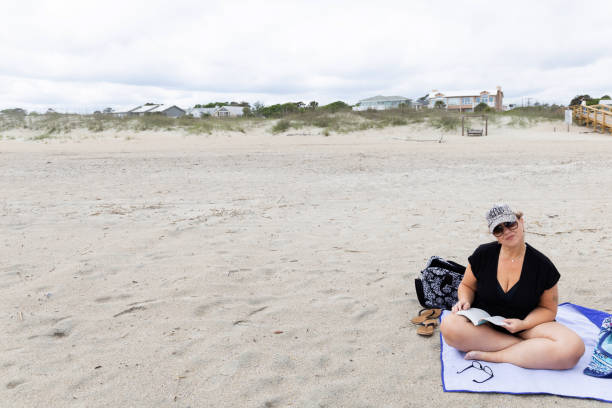 istock a woman sitting on the beach alone reading a book 1327522738