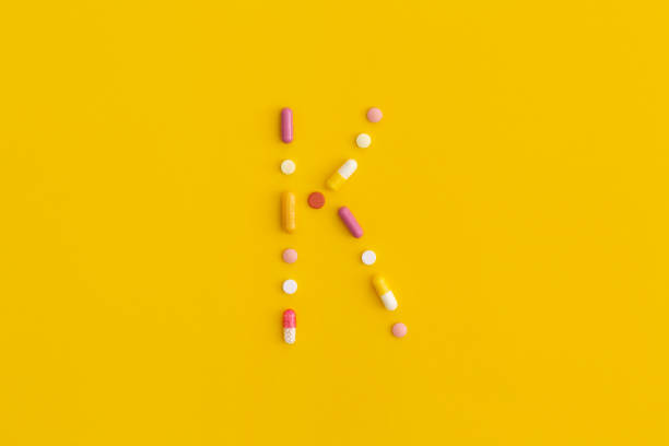 vitamina k hecha de pastillas sobre fondo amarillo. vista superior con espacio de copia. lay plana. - capsule vitamin pill letter k medicine fotografías e imágenes de stock