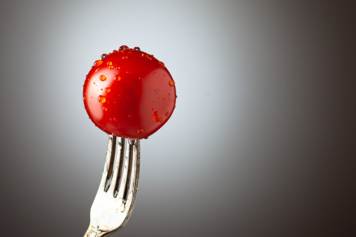 small cherry tomatoes in drops of water on a silver fork. Gradient background. Place under the text. Copy space