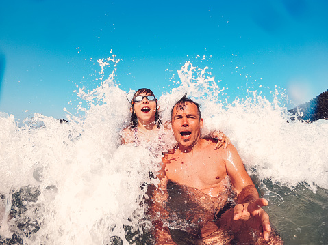 Father and daughter swimming in the sea and having fun on the beach while having splashed by the big wave