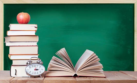 Open book with watch, red apple and stack of books on the blackboard background