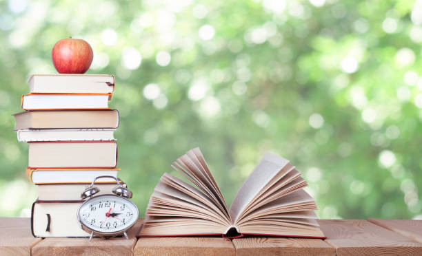 Open book with watch, red apple and stack of books on the nature background