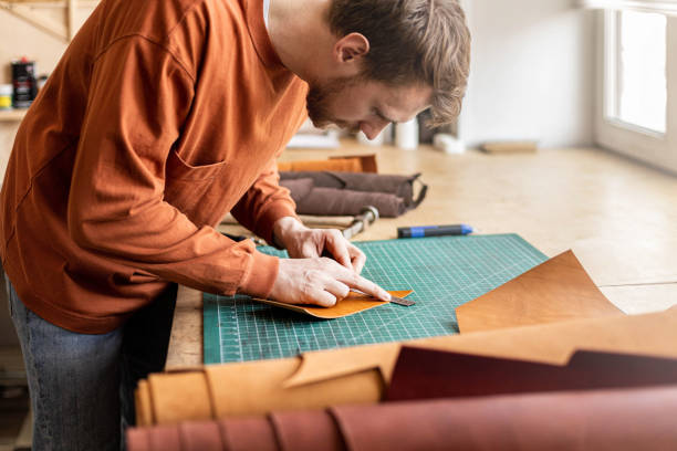 Male tanner making cutting scheme of bag working at leather workshop. Handcrafted creating