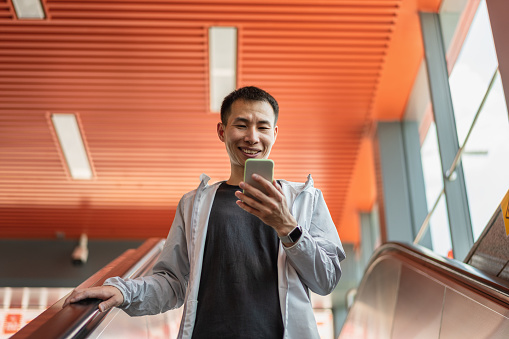 Asian man uses his smartphone to view information while smiling while riding the escalator