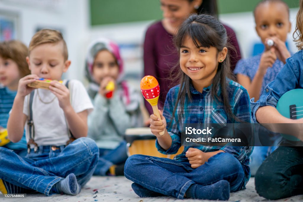 Kids playing music in preschool A diverse group of children sits on the carpet and play musical instruments. They are smiling, having a good time. Music Stock Photo
