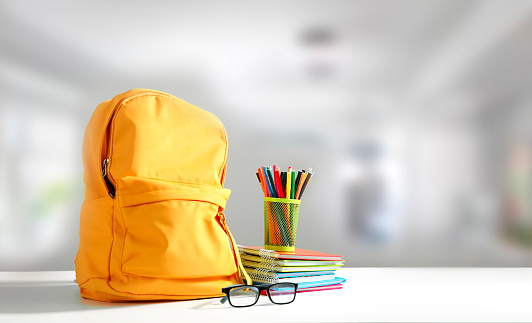 Yellow backpack on table empty copy space. School supplies. Education objects. School bag and stack of notebooks.