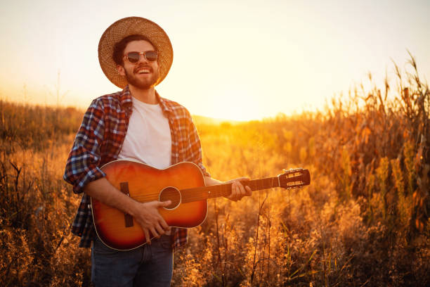 wesoły przystojny mężczyzna grający na gitarze na świeżym powietrzu podczas zachodu słońca - acoustic guitar guitarist country and western music guitar zdjęcia i obrazy z banku zdjęć