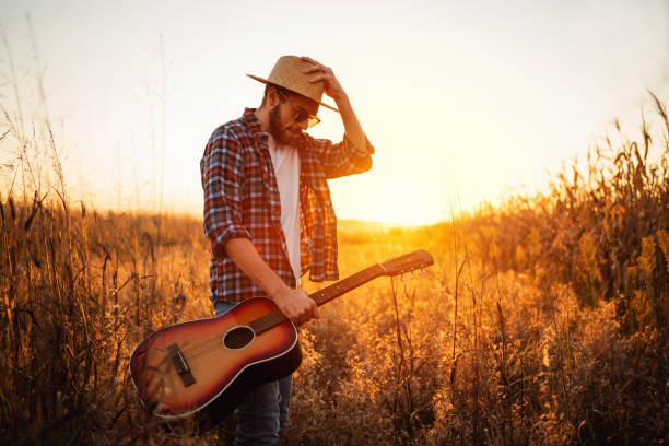 istock Young man with guitar walking on the field 1327551433