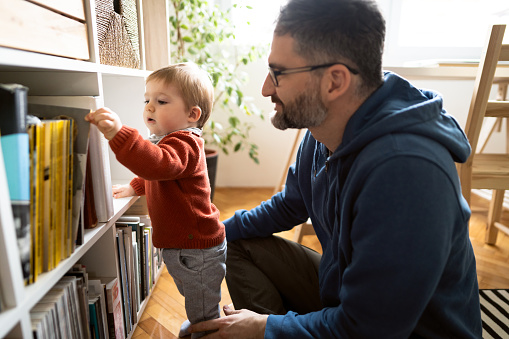 Caucasian father spending quality time with his baby son at home. Father rearranges the shelves in the house with his little son.