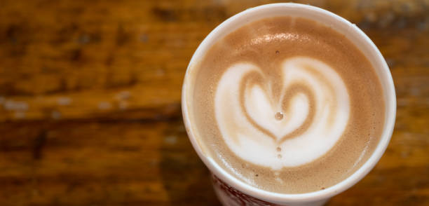 Table top view of a paper cup of hot latte coffee on wooden table.