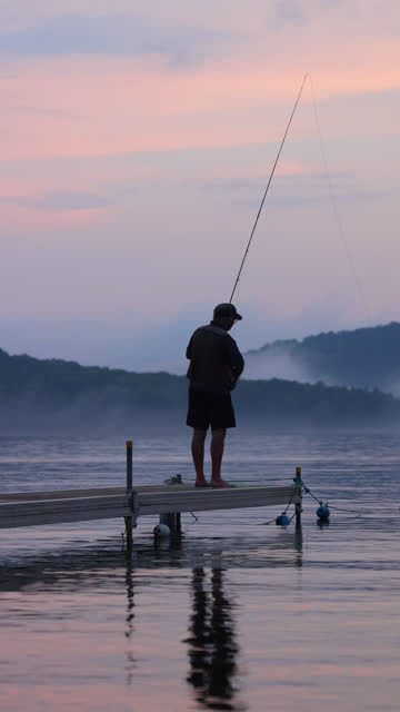 Vertical video of Senior Man Fly-Fishing at Sunset at the lake. He is standing on a pier at Lac St-Joseph, Quebec, Canada.