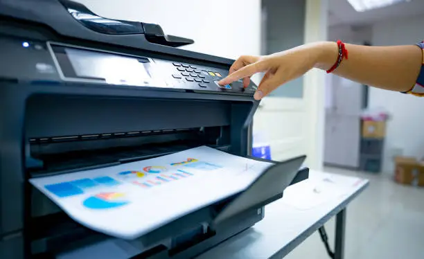 Office worker prints paper on multifunction laser printer. Copy, print, scan, and fax machine in office. Document and paper work. Print technology. Hand press on photocopy machine. Scanner equipment.