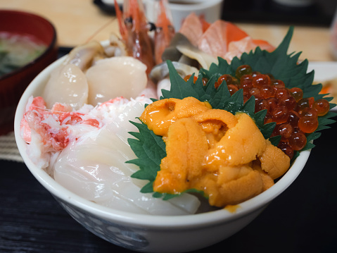 closeup selective focus various fresh seafood topped on rice bowl in Japanee style, uni (sea urchin), salmon roe (eggs), hotate (scallops), crab meat and shrimps