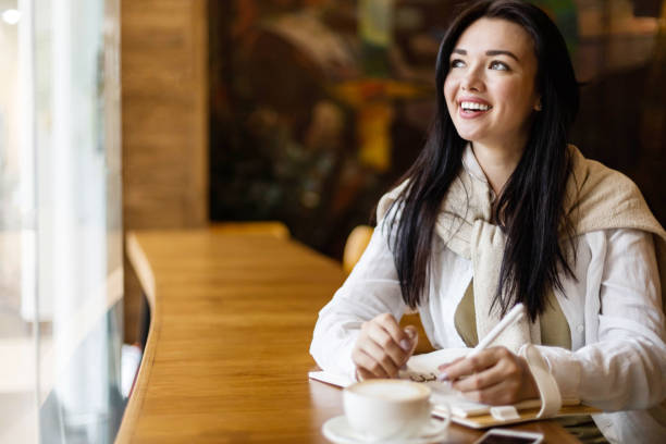 istock Happy Asian young woman sitting at cafe with coffee cup taking notes enjoying break 1327576595
