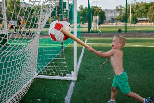 Photo of Preschool boy hits pinata from cardboard and color paper with wooden stick, part of birthday party