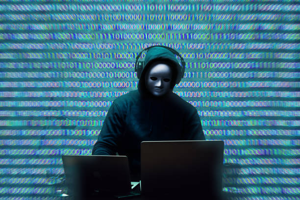 Anonymous hacker wearing face mask working on computer in dark room Anonymous hacker wearing face mask working on computer in dark room, close up anonymous activist network stock pictures, royalty-free photos & images