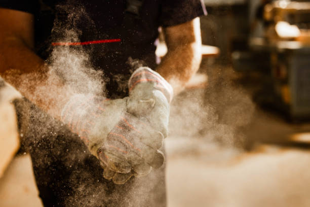 Close up of unrecognizable worker cleaning dust from his gloves. Close up of unrecognizable manual worker cleaning sawdust from his protective gloves in a workshop. repairperson occupation stock pictures, royalty-free photos & images