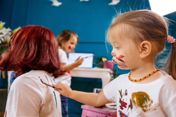 istock Family hobbies leisure activity home concept. Mother and small daughter drawing with fun using paintbrushes and watercolors. Children and parent creating picture together, body paint, home quarantine. 1327586437