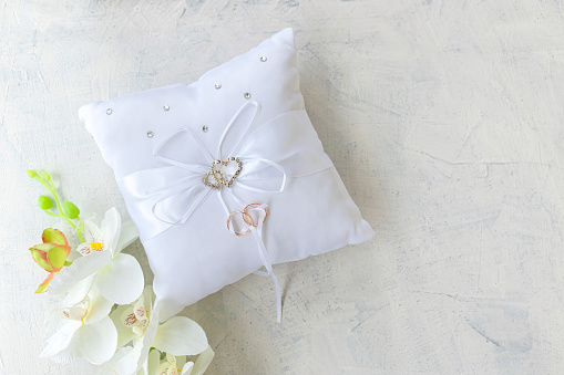 pillow for wedding rings with rings with rhinestone hearts and white orchid on a white texture background. fla tlay top view soft focus