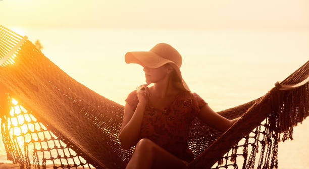 Vacation Beach Summer Holiday Concept. Young pretty woman in hat sitting in hammock at sunset stock photo