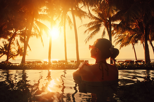 Vacation Beach Summer Holiday Concept. Silhouette beautiful woman relaxing in swimming pool on summer beach resort watching sunset.