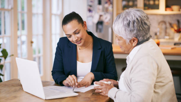 foto de un consultor pasando por el papeleo durante una reunión con una mujer de la tercera edad en casa - insurance agent fotografías e imágenes de stock