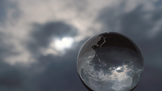 World map etched onto a glass sphere with a turbulent sky refracted in it.