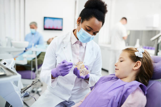 dentista afroamericano che usa il modello dentale mentre parla con una bambina durante l'appuntamento nello studio del dentista. - igienista dentale foto e immagini stock