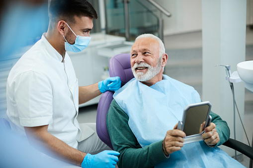 Hombre mayor satisfecho que comunica con su dentista después de procedimiento dental en la oficina del dentista. photo
