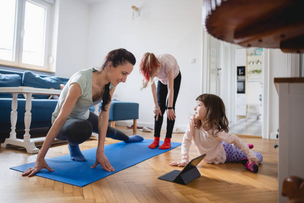 istock Smiling mother exercising and watching tutorial on laptop, her daughters playing around 1327592148