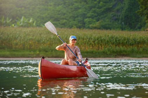Woman smiling while floating on a kayak on the river in the countryside.